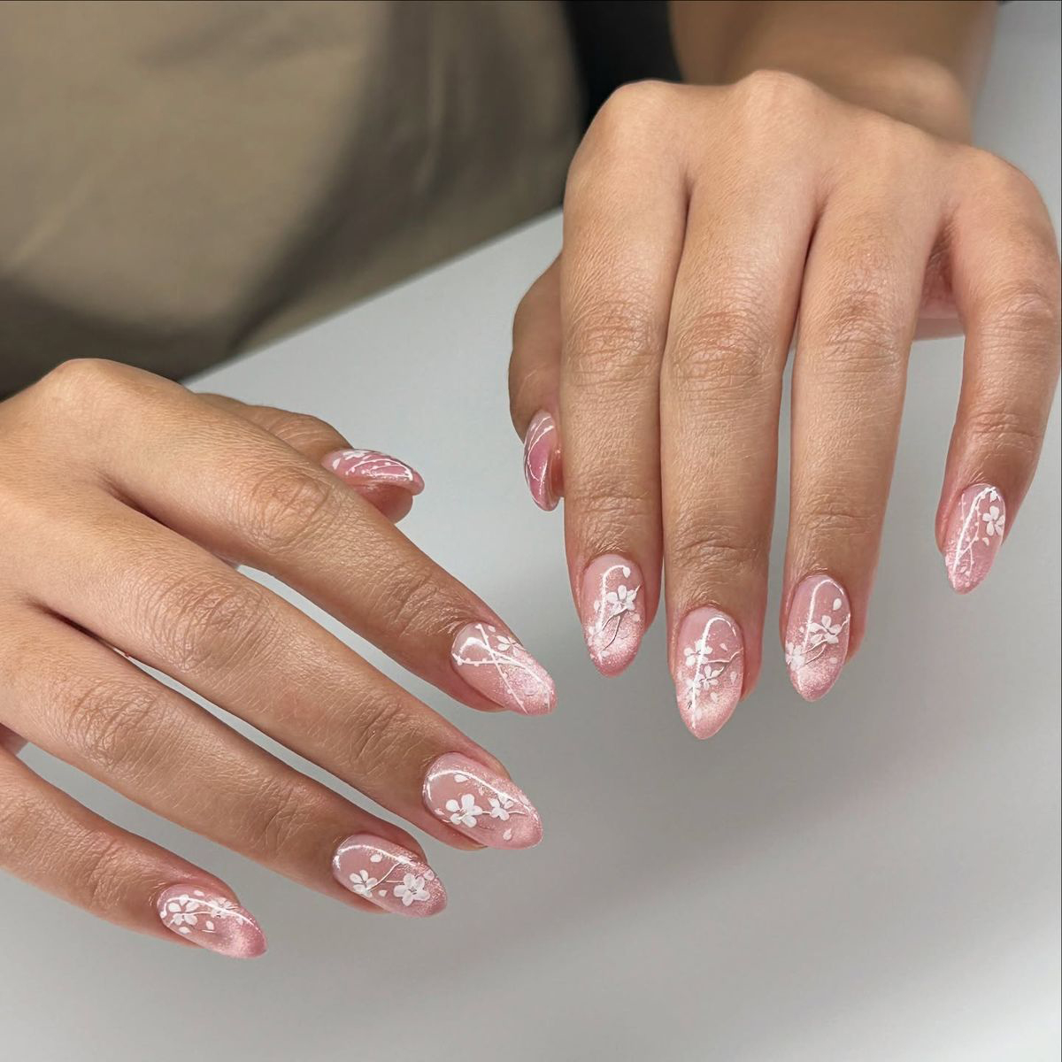 Soft pink magnetic cat-eye nails with delicate hand-painted white cherry blossoms and almond shape