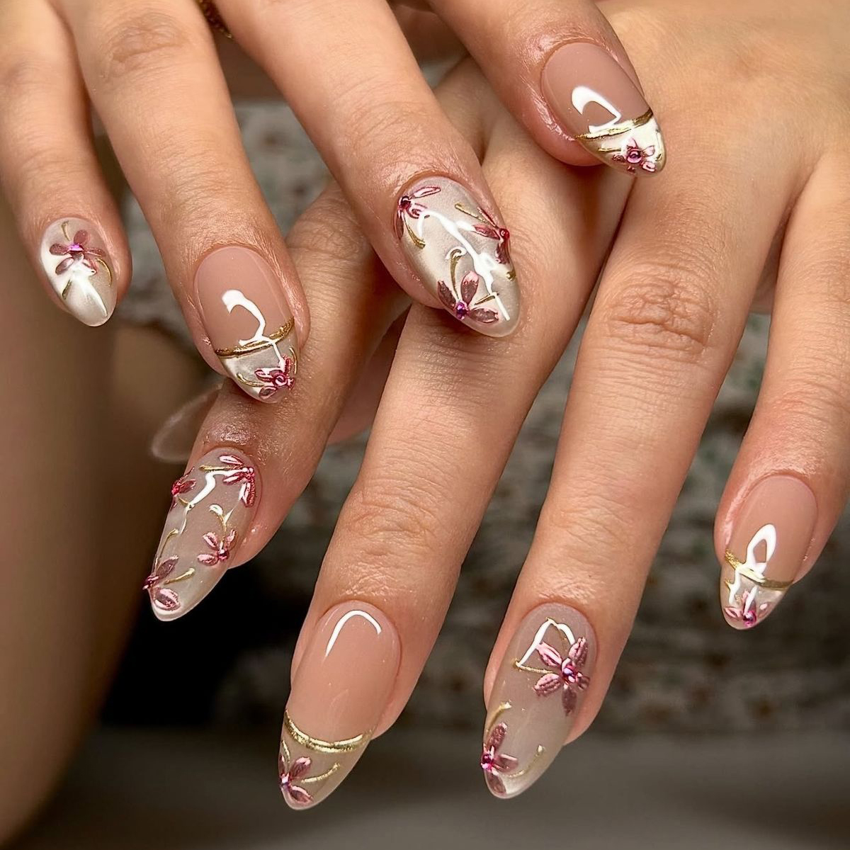Nude almond nails featuring white French tips with gold ribbon accents and delicate pink rhinestone flowers