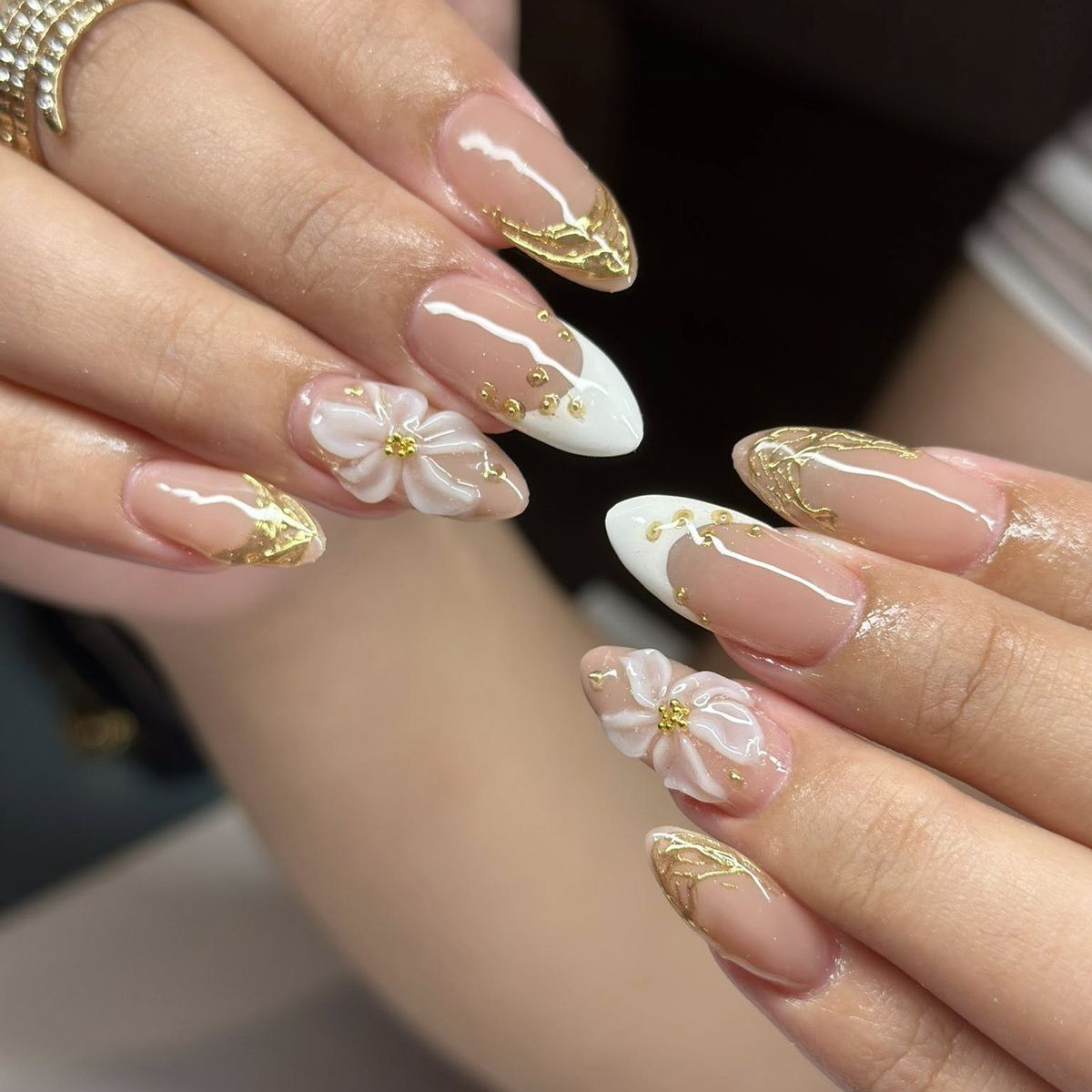 Elegant almond nails with white French tips, intricate gold filigree art, and 3D white embossed flowers with pearl centers