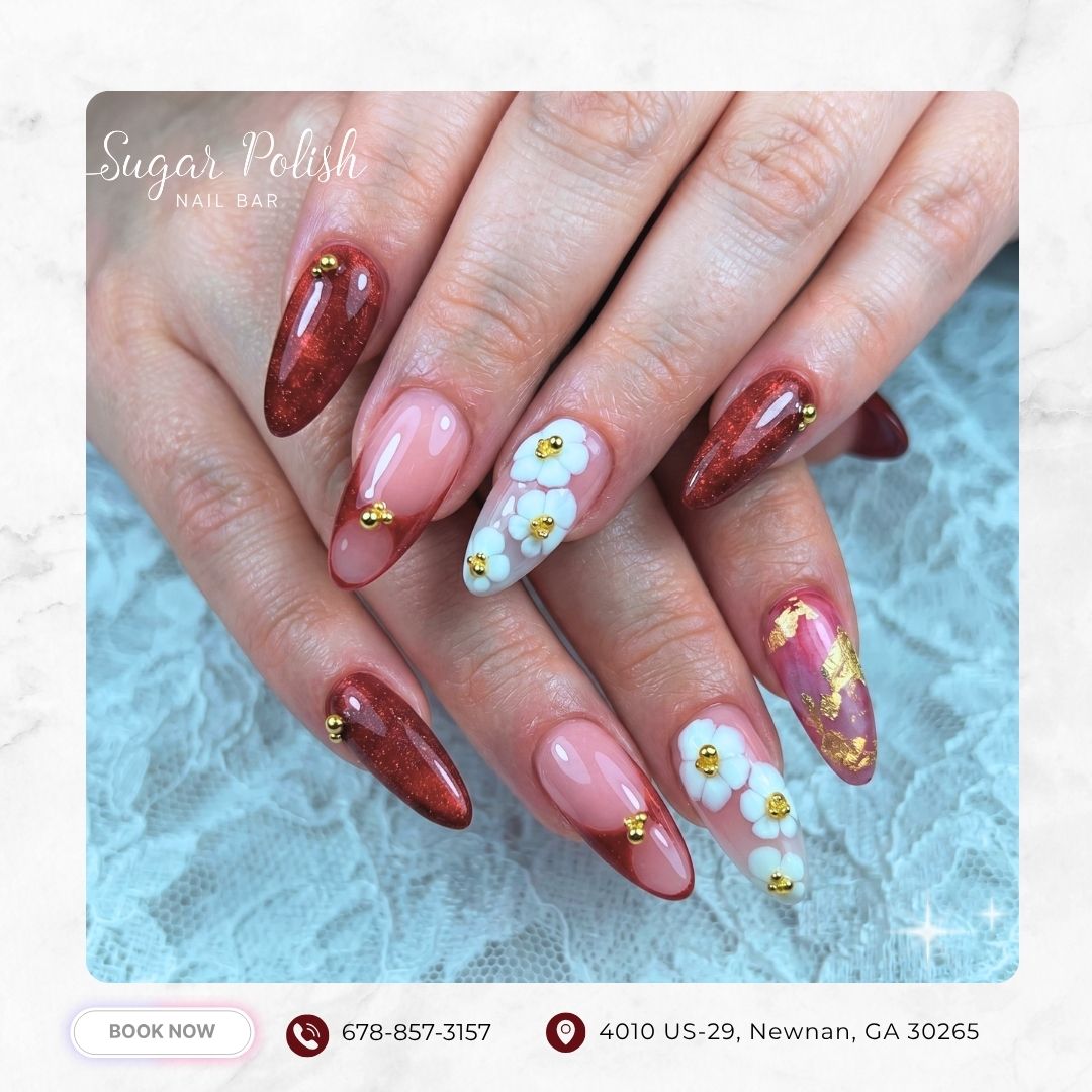Red and nude almond nails with 3D white flowers, gold studs, and marble accents