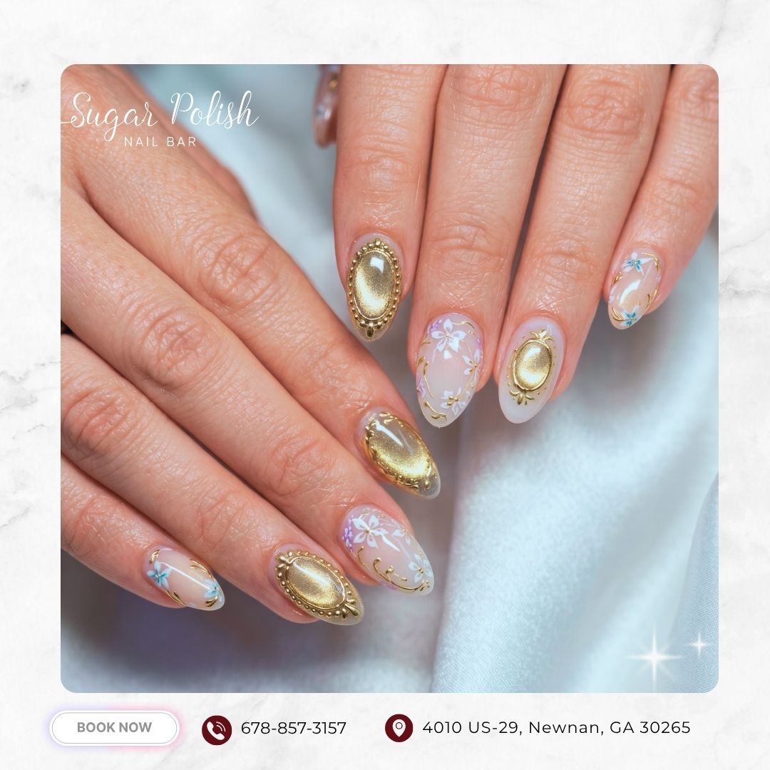 Almond nails with white floral art, gold embellishments, and elegant nude base