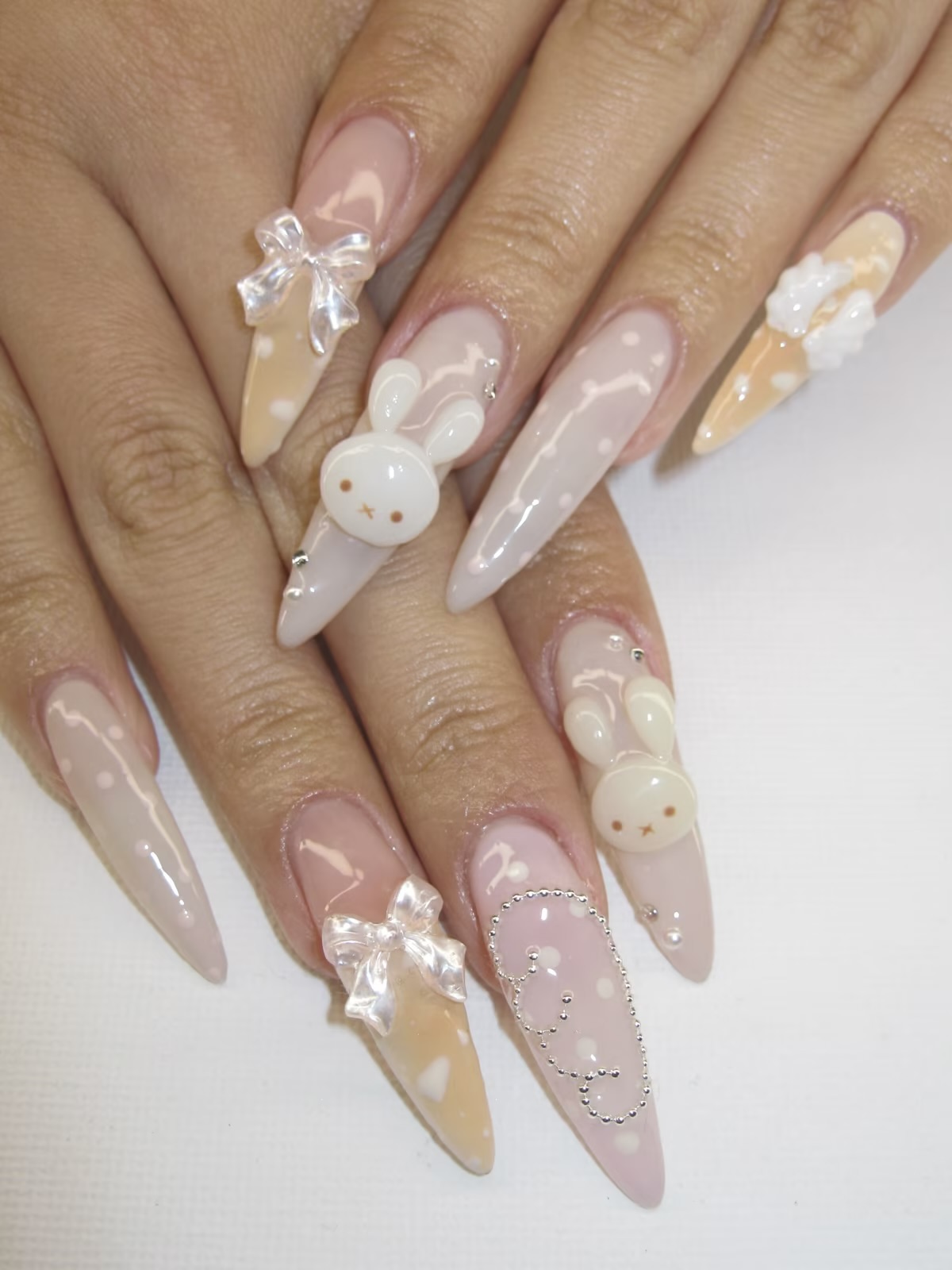 Close-up of playful pastel Easter nail art on almond nails, featuring a mix of lavender, mint, yellow, and peach French tips, a cute white bunny face, and a tiny carrot design on accent nails.