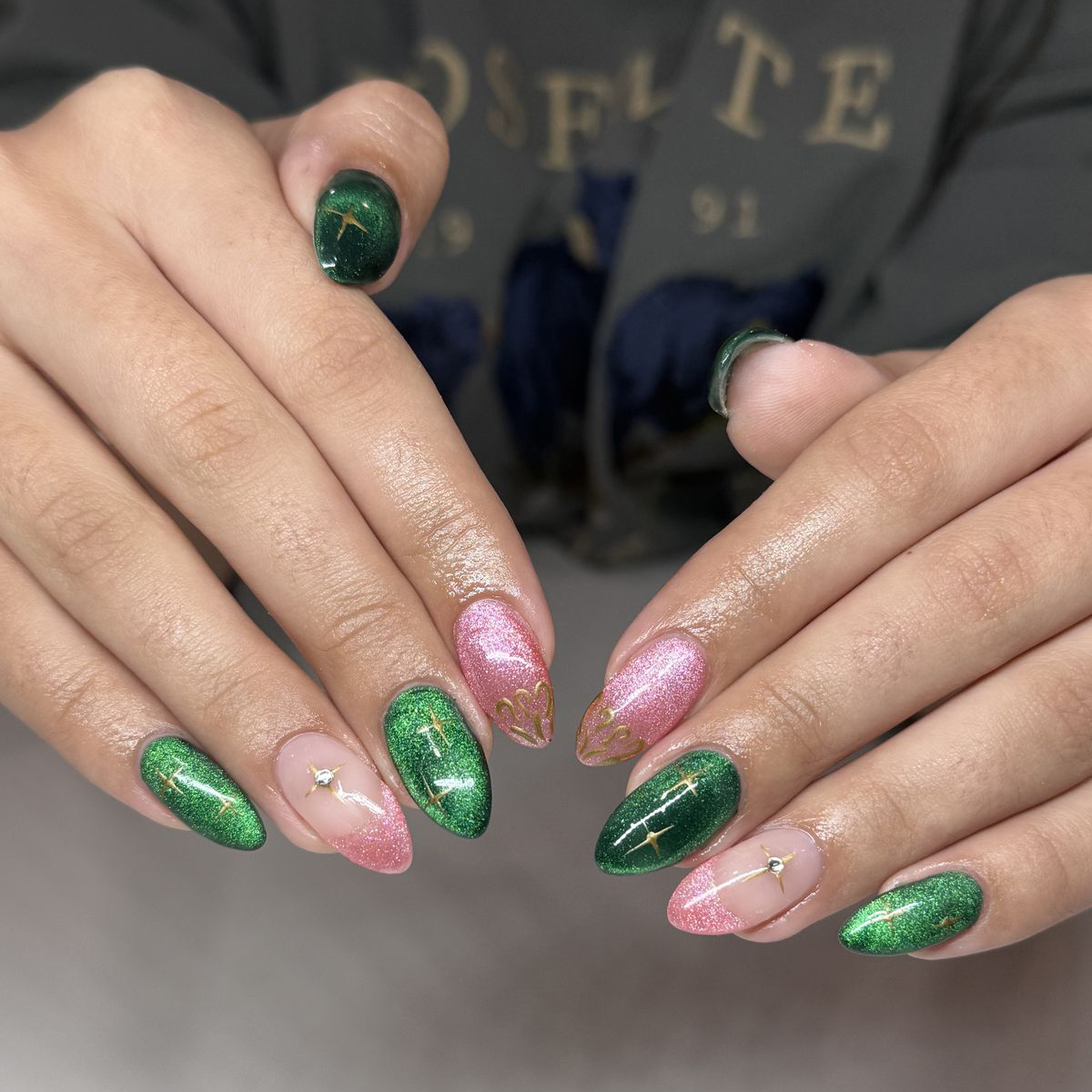 Deep emerald green and sparkling pink glitter almond nails with gold star decals and intricate filigree art